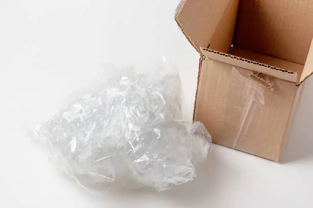 A lump of crumpled cellophane packing filler next to an open cardboard box. Safety of parcels and things during transportation and storage