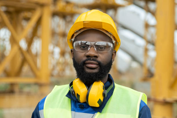 Young African engineer in workwear looking at you Young African engineer in workwear and protective helmet looking at you protective eyewear stock pictures, royalty-free photos & images