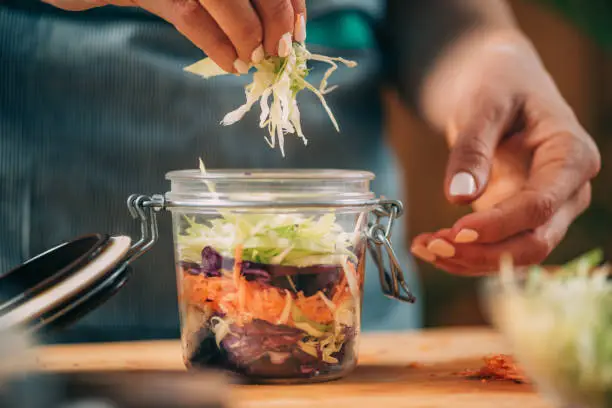 Fermenting vegetables. Woman putting cabbage and carrots in the jar, preparing them for fermentation.