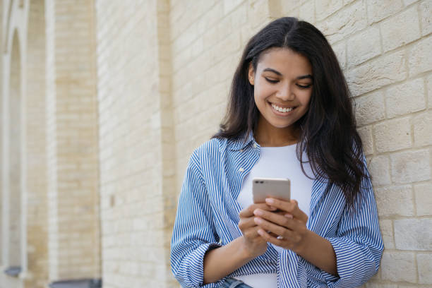 istock Smiling woman holding smartphone, using mobile app for online shopping standing outdoors, copy space. Young happy African female communication online, watching videos, reading news 1323169901