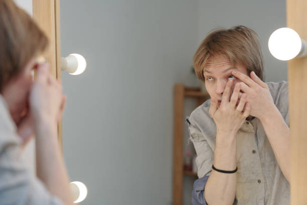 istock Young man putting contact lens in front of mirror 1323172372
