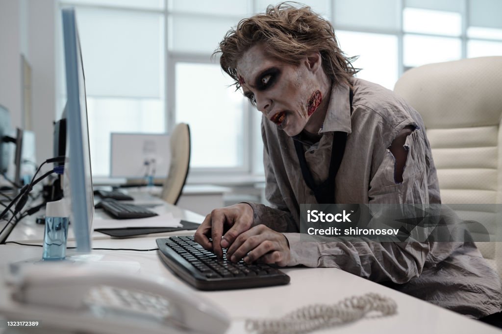Ugly man with zombie makeup working with computer Ugly man with zombie makeup working with computer in office Zombie Stock Photo