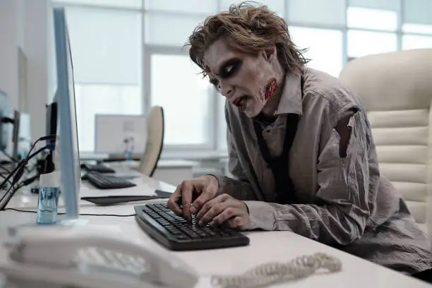 Photo of Ugly man with zombie makeup working with computer