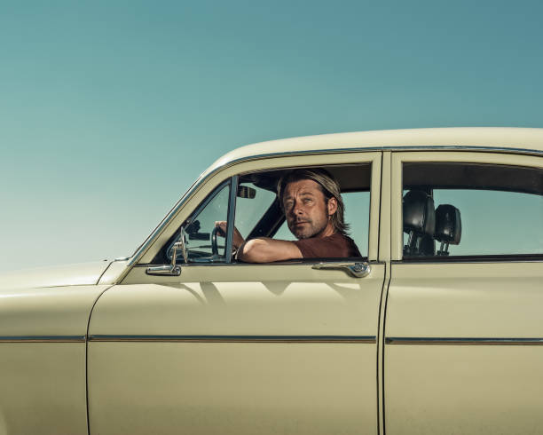 istock Blond man in t-shirt in classic car looking out open window. 1323179712