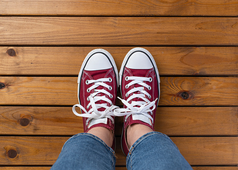 Women's feet in red sneakers on wooden pier floor with copy space