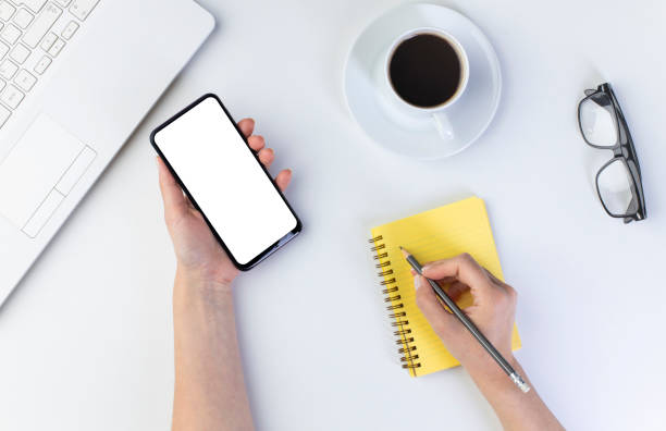 istock Woman hands holding smartphone at office desktop, top view 1323183995