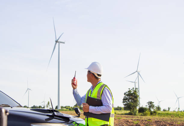 istock front view Asian engineer smiling holding folder looking at camera with windmill, wind turbine power background. 1323184573