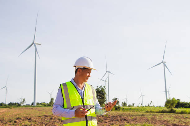 istock front view Asian engineer smiling holding folder looking at camera with windmill, wind turbine power background. 1323184603