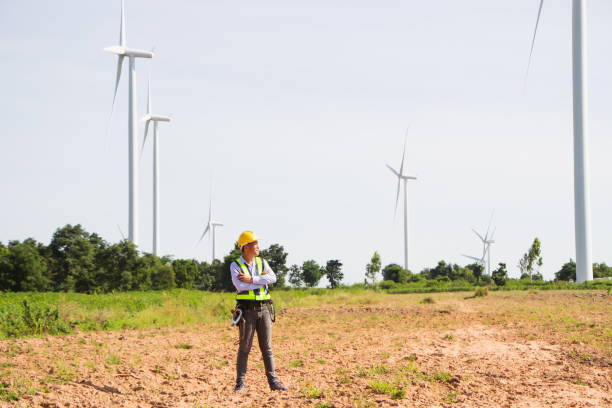 istock front view Asian engineer smiling holding folder looking at camera with windmill, wind turbine power background. 1323184778
