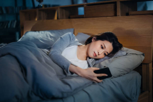 istock Young Asian woman checking her smartphone while lying on bed before bedtime, spending a chilling night at cozy home 1323184908