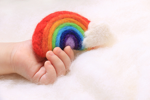 A child's hand holding a little felt rainbow.