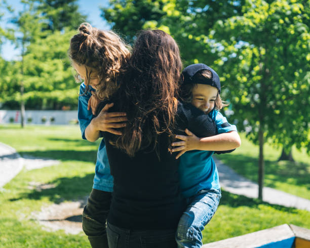istock Mother embraces two sons in sunny city park 1323201864