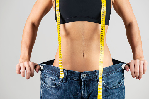 Belly of an unrecognizable slim caucasian woman wearing an oversized jeans and is showing how big the pants are. Representing being healthy and slim after regular workout and healthy lifestyle.
Image is not body shape retouched