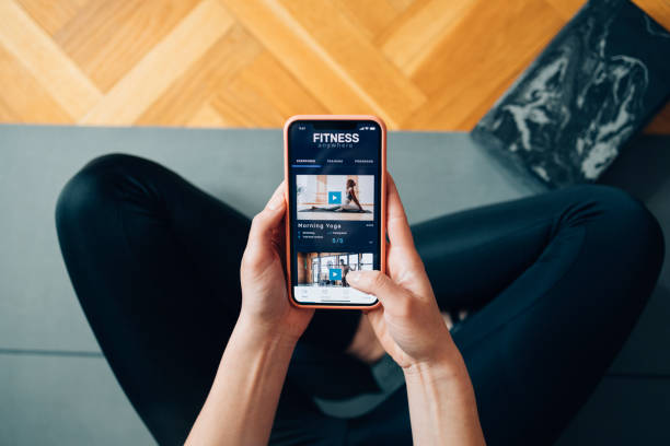 séances d’entraînement à domicile: femme anonyme suivant un cours de yoga sur son téléphone portable - floor women sitting yoga photos et images de collection