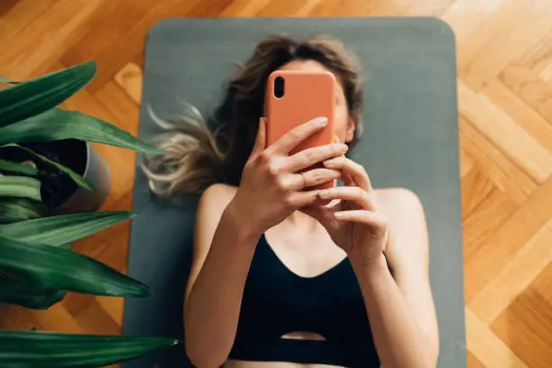 Photo of Young Woman Lying on a Yoga Mat and Using Her Smartphone