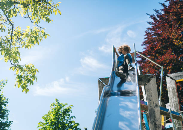 il ragazzo scivola giù scivola giù per lo scivolo nel parco giochi - children only tree area exploration freshness foto e immagini stock