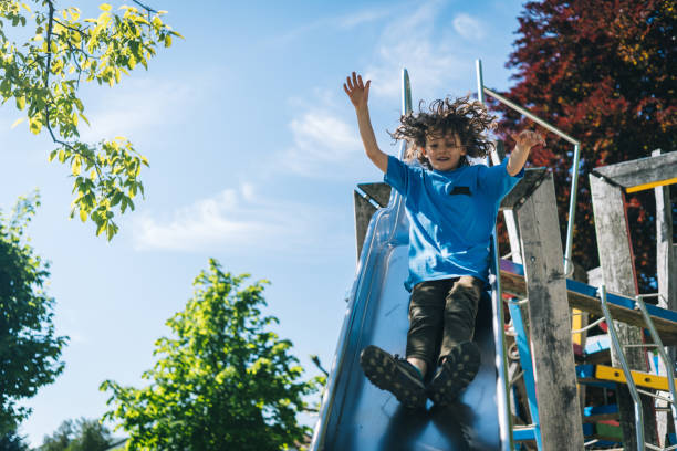 istock Young boy slides down slide at playground 1323203980