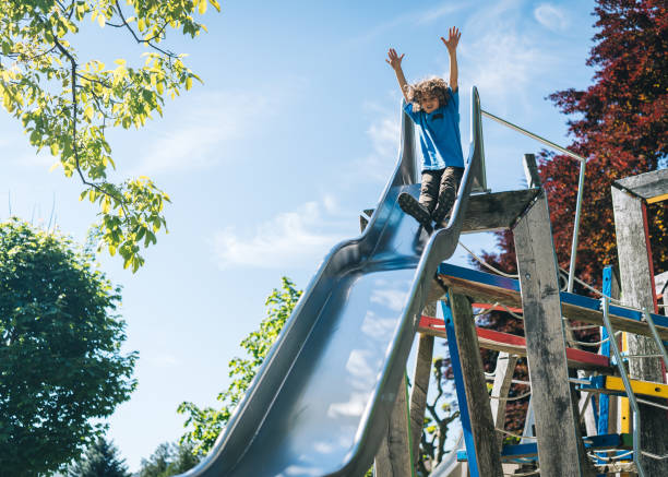 istock Young boy slides down slide at playground 1323203988