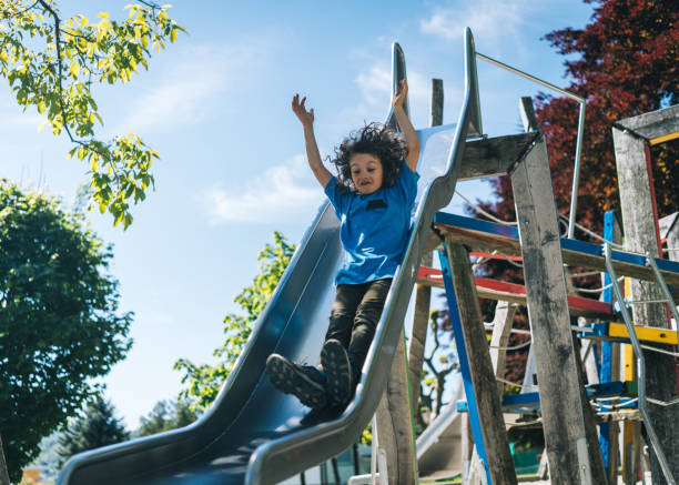 istock Young boy slides down slide at playground 1323203995