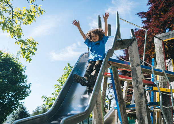 young boy slides down slide at playground - children only tree area exploration freshness imagens e fotografias de stock