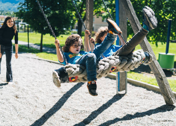 istock Mother pushes young boys on swings at playground 1323204024