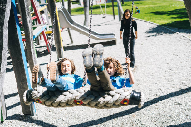 istock Mother pushes young boys on swings at playground 1323204171