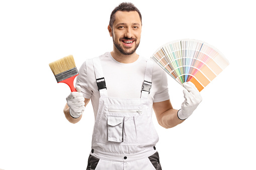 The builder, a Caucasian man, holds a paint roller and a tin can of paint in his hands