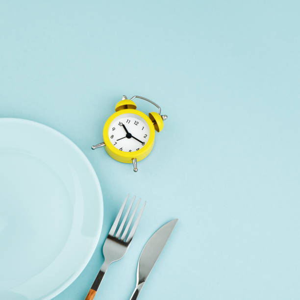 istock Intermittent fasting, diet, lunch time concept. Yellow alarm clock, empty plate and cutlery on a blue background. 1323207156