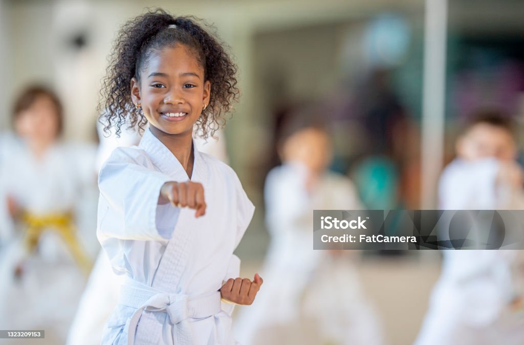 Young karate class A young African American girl practices karate in a class setting and smiles at the camera. Karate Stock Photo