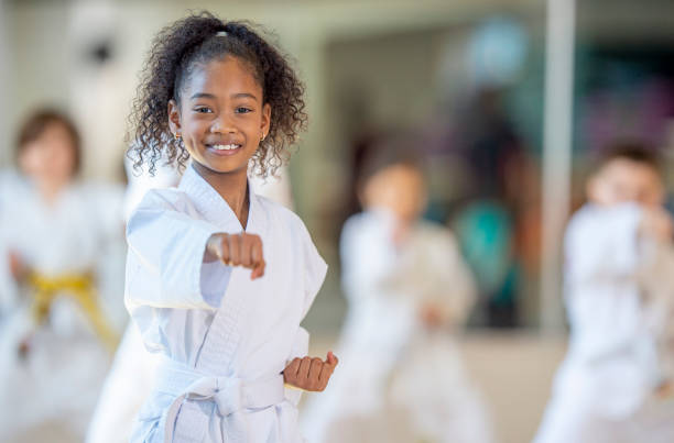 Young karate class A young African American girl practices karate in a class setting and smiles at the camera. martial arts stock pictures, royalty-free photos & images
