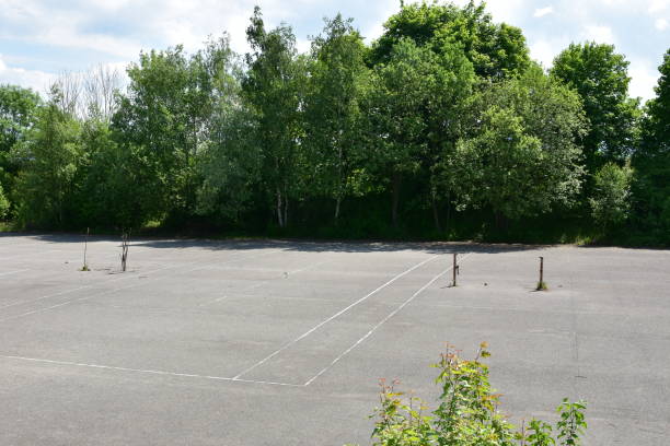 istock Old abandoned, desolate concrete hard tennis courts surrounded by trees and bushes under blue sky. 1323209974