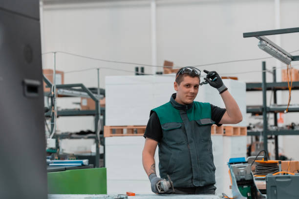 istock Heavy Industry Engineering Factory Interior with Industrial Worker Using Angle Grinder and Cutting a Metal Tube. Contractor in Safety Uniform and Hard Hat Manufacturing Metal Structures. 1323216689