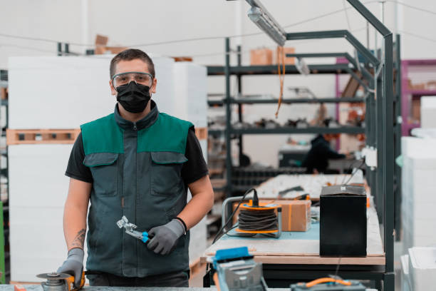 istock Heavy Industry Engineering Factory Interior with Industrial Worker Using Angle Grinder and Cutting a Metal Tube.He Wears a Mask on His Face Because of the Coronavirus Pandemic 1323218488