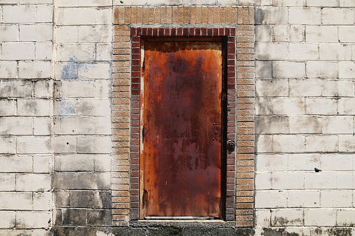 A rusty red old metal steel door in a back alley concrete block abandoned warehouse building.