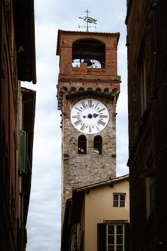 Famous Torre delle Ore (tower of the hours), ancient medieval turret clock in the town center of Lucca (Tuscany, Italy), landmark and symbol of the city seen from the nearby narrow alleys