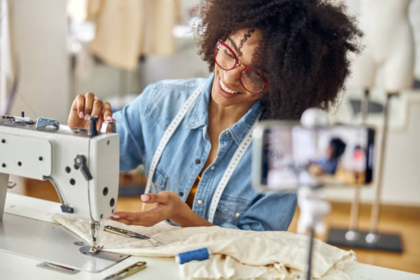 istock Smiling African-American seamstress adjusts sewing machine shooting new video in studio 1323232774