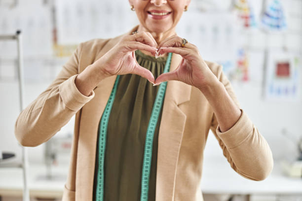 istock Middle aged lady designer with tape measure shows heart with hands in spacious studio 1323232834