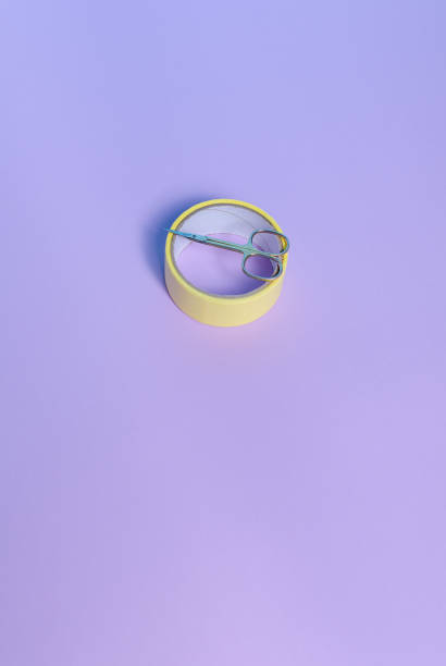 istock Small scissors and yellow scotch tape on a purple background. 1323233666