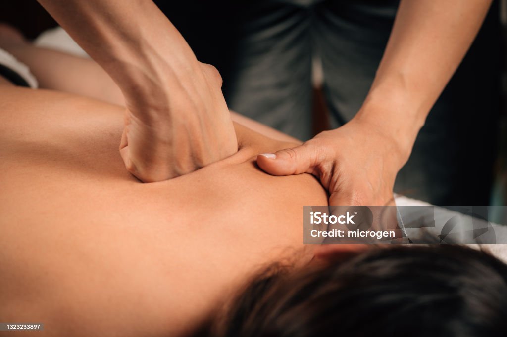 Deep Tissue Massaging. Deep tissue massaging therapy. Therapist hands massaging woman’s shoulder Massaging Stock Photo