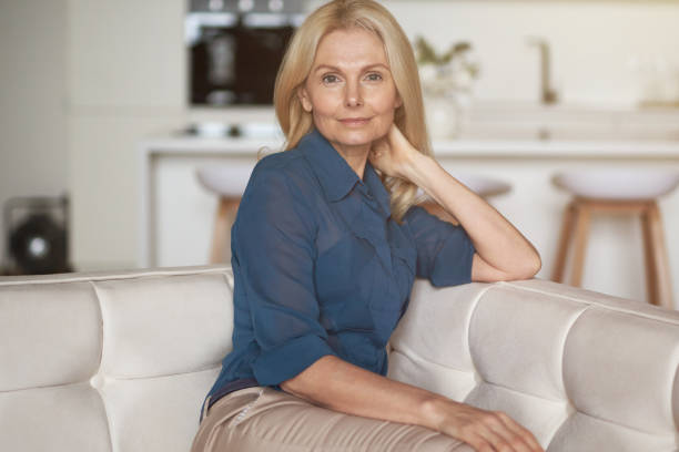 istock Attractive mature woman with pleasant smile looking at camera while relaxing, sitting on sofa in her modern apartment 1323233939
