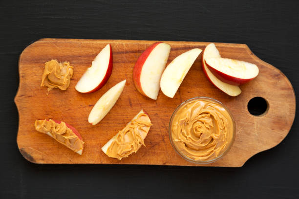 istock Raw Red Apples and Peanut Butter on a rustic wooden board on a black background, top view. Flat lay, overhead, from above. 1323233964