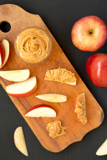 istock Raw Red Apples and Peanut Butter on a rustic wooden board on a black background, top view. Flat lay, overhead, from above. 1323233997