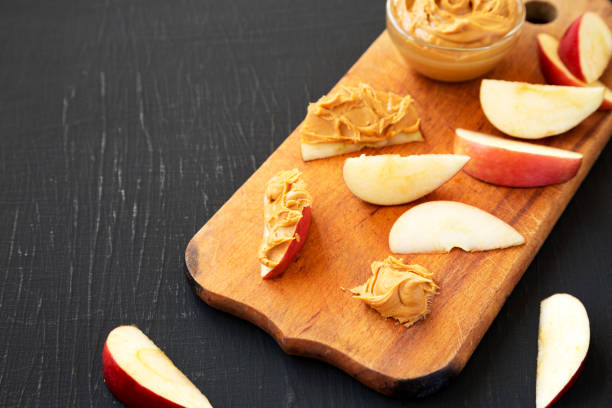 istock Raw Red Apples and Peanut Butter on a rustic wooden board on a black background, low angle view. Copy space. 1323234014