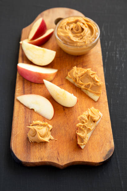 istock Raw Red Apples and Peanut Butter on a rustic wooden board on a black surface, side view. 1323234023