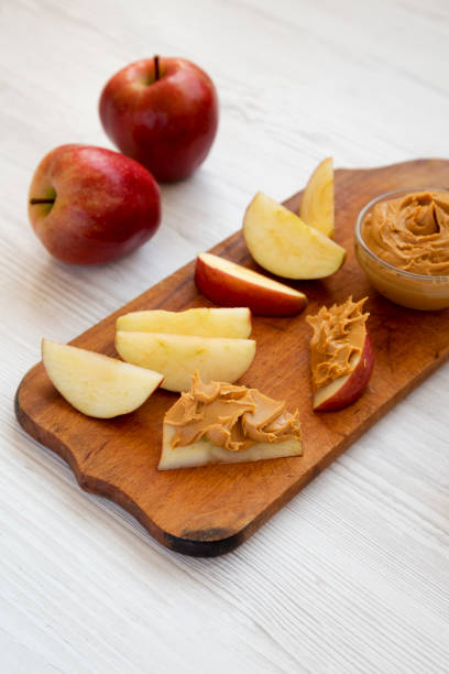 istock Raw Red Apples and Peanut Butter on a rustic wooden board on a white wooden surface, side view. 1323234101