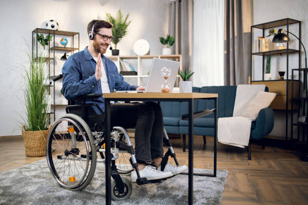 istock Man in wheelchair using headset and laptop for video call 1323236052