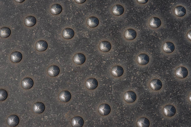 Closeup of a used metal plate with studs as a crossing marker for blind people. Closeup of a metal plate with studs as a crossing marker for blind people. \nThe plate is placed in the sidewalk of a Dutch city.