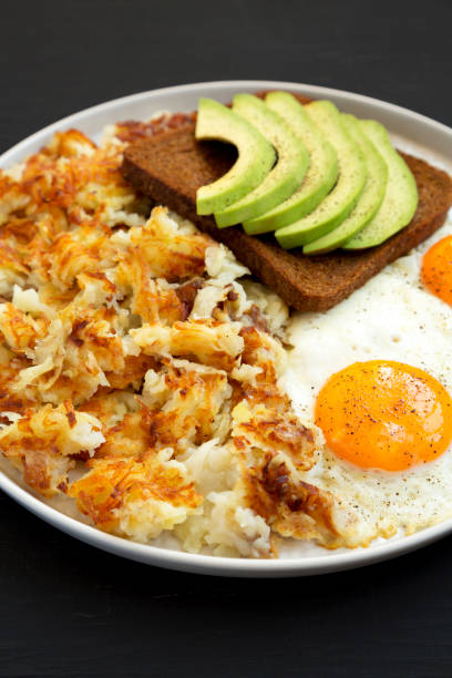 sabrosos hashbrowns fritos caseros y huevos en un plato sobre un fondo negro, vista de ángulo bajo. primer plano. - hash brown gold food vegetable fotografías e imágenes de stock