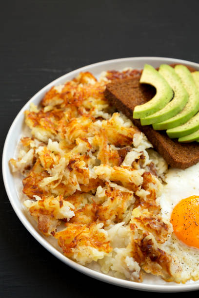 sabrosos hashbrowns fritos caseros y huevos en un plato sobre un fondo negro, vista de ángulo bajo. - hash brown gold food vegetable fotografías e imágenes de stock