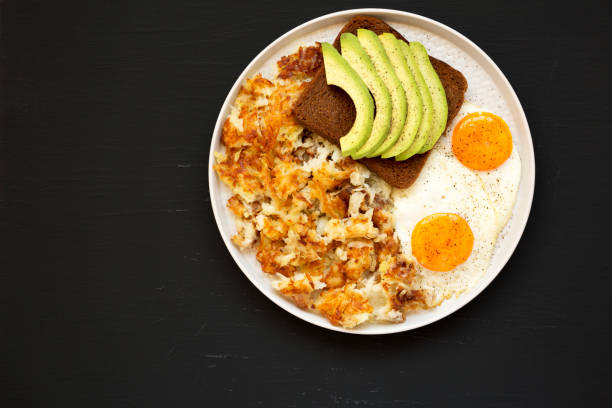 sabrosos hashbrowns fritos caseros y huevos en un plato sobre un fondo negro, vista superior. espacio de copia. - hash brown gold food vegetable fotografías e imágenes de stock